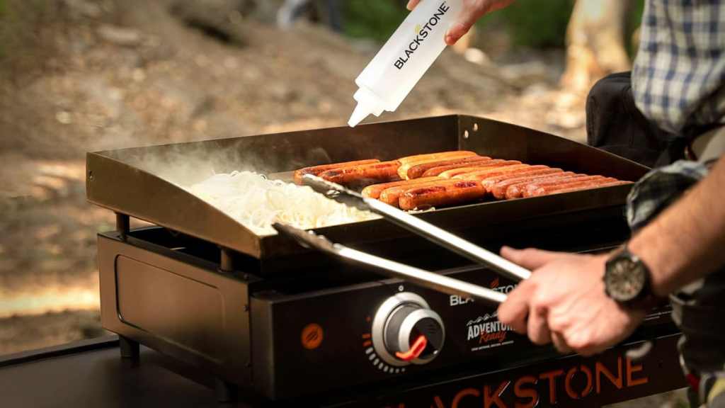 cooking on a blackstone griddle holding griddle bottle and tongs